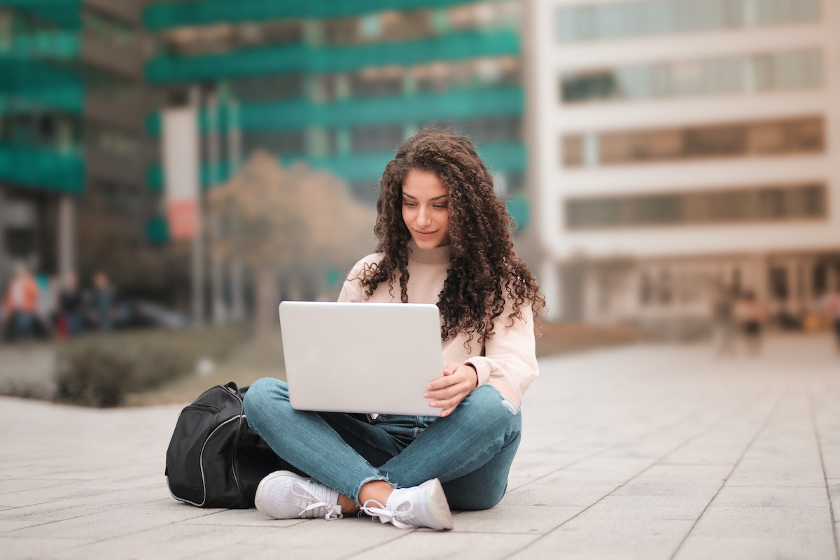 Jovem estudante sentada no chão, com o notebook no colo enquanto confere informações sobre Dívida do FIES 2024