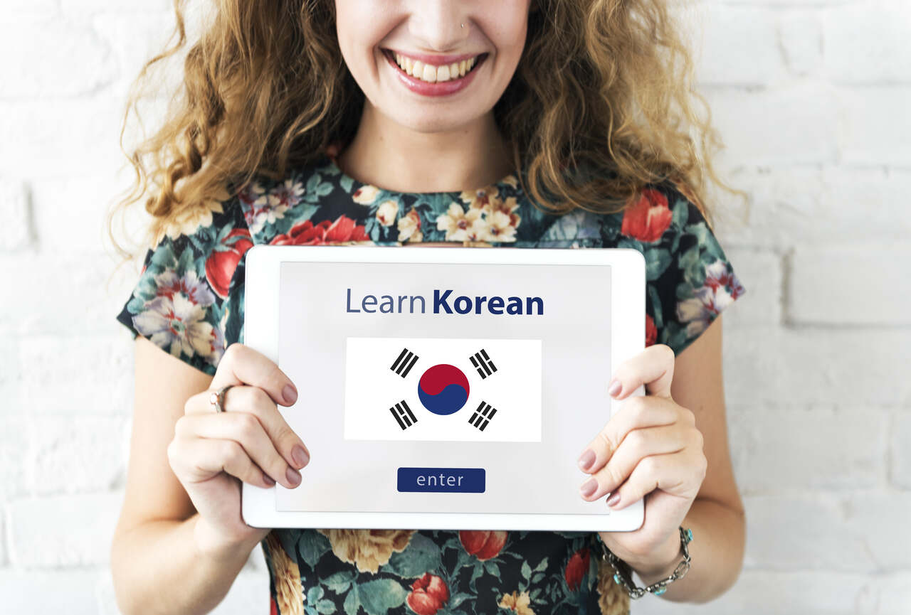 mulher mostra tela de um tablet  com bandeira da Coréia do Sul escrito aprender coreano