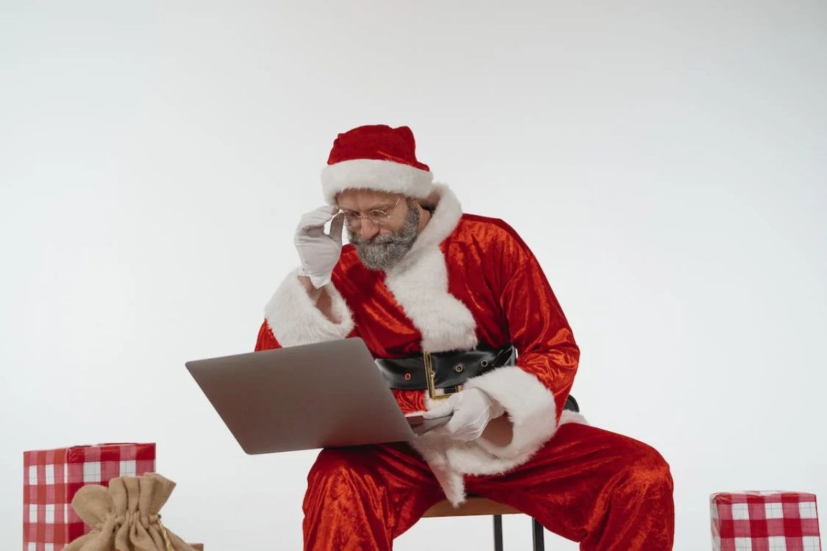 Um papai Noel sentado enquanto olha um notebook apoiado em sua perna