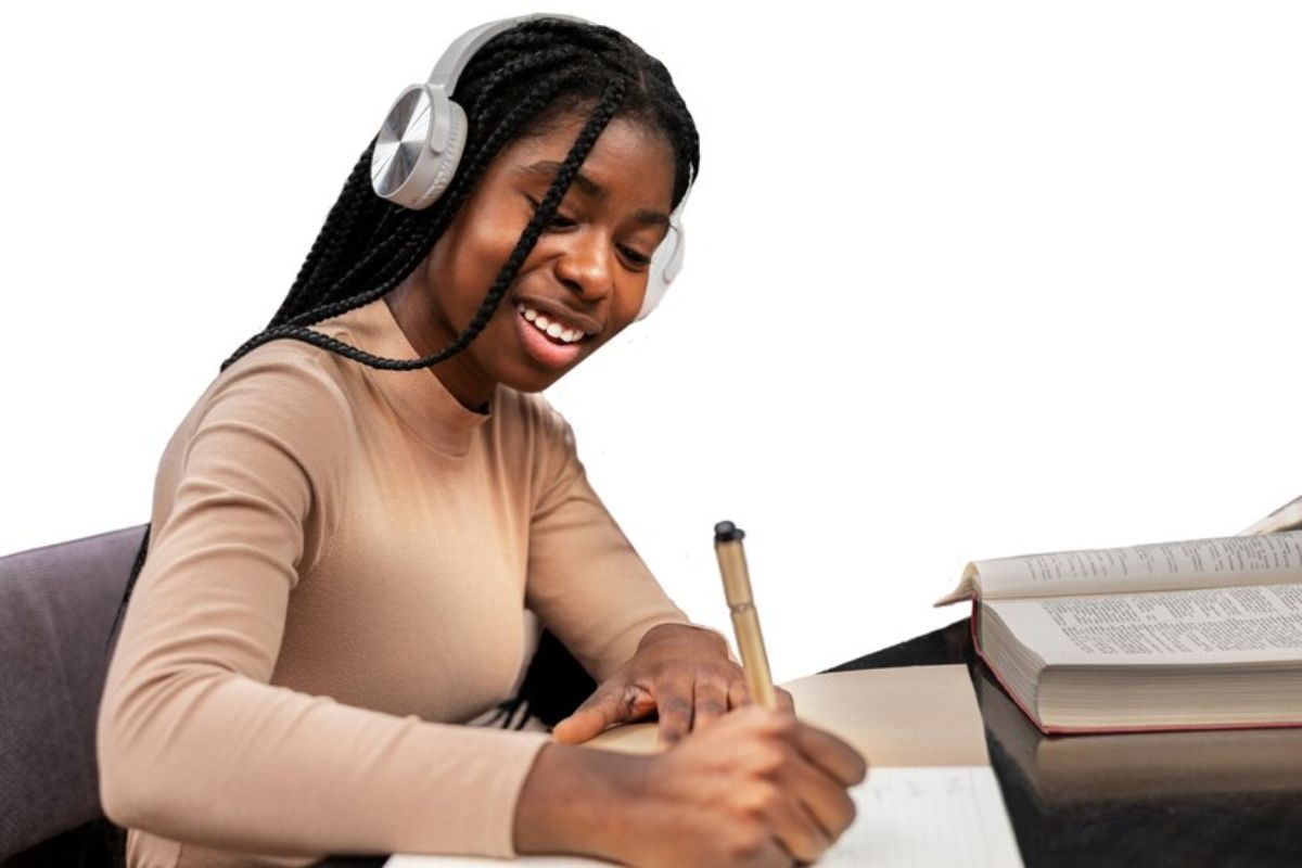 Uma aluna faz anotações em seu caderno. Ela sorri e ouve música em um headphone