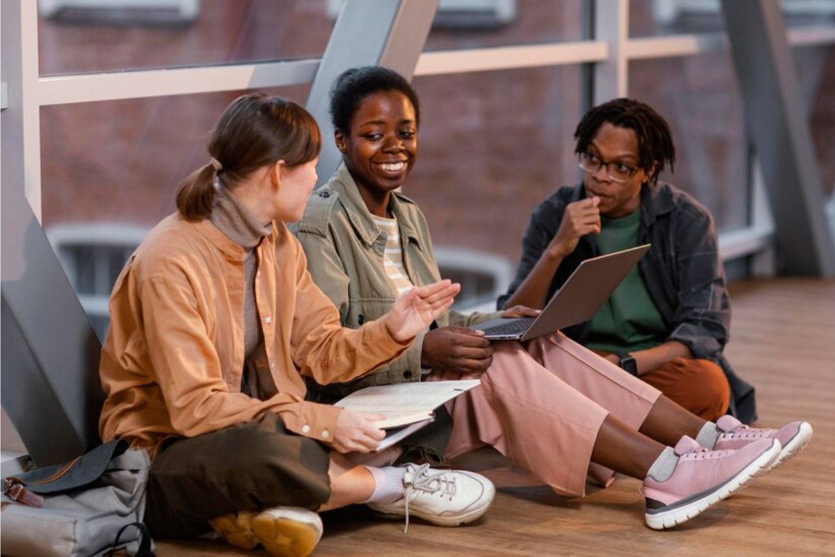 Três alunos no corredor da universidade conversam sentados