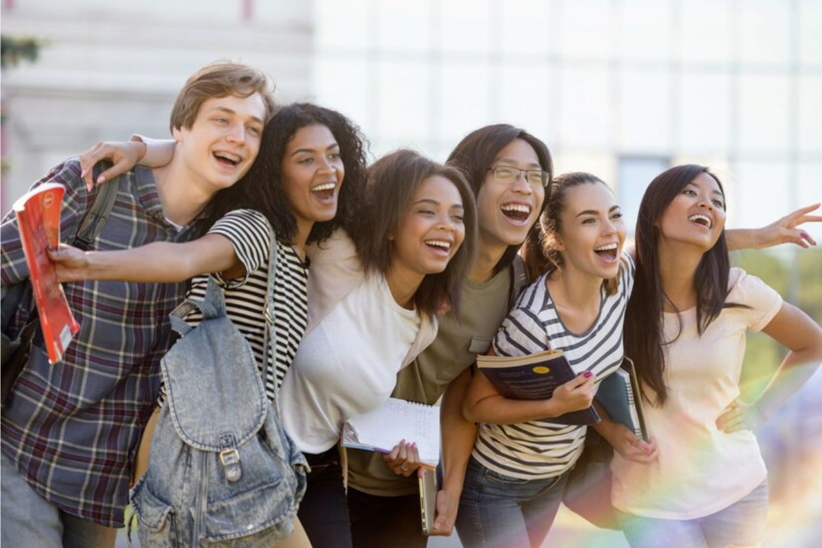Um grupo de alunos sorri na frente da faculdade após a aprovação