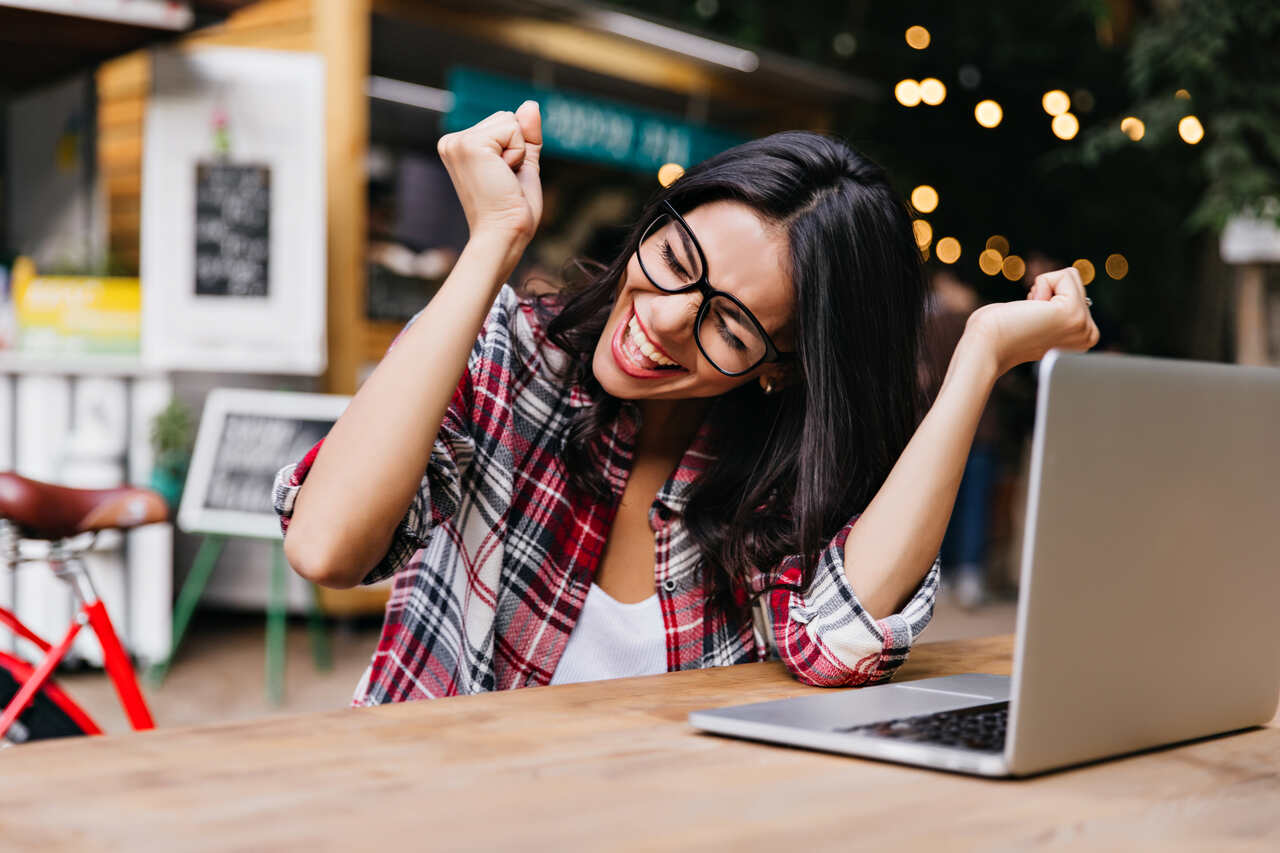 Jovem comemora algo que acaba de verificar no notebook a sua frente