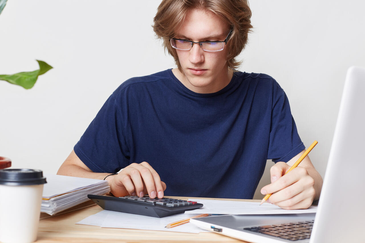 jovem faz contas em uma calculadora sentado diante o notebook