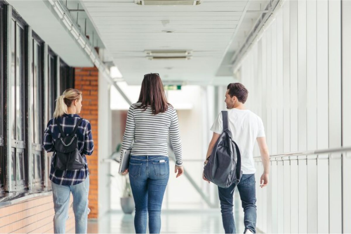 Três alunos vistos de costas no corredor da faculdade após verem Como Funciona o ProUni 2025