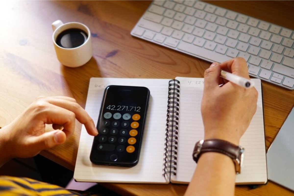 Uma pessoa usa a calculadora de seu celular. O celular está em cima do seu caderno onde ele faz algumas contas para Calcular Nota do ENEM 2025