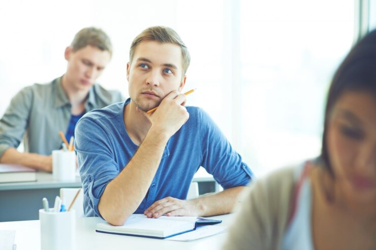 Um aluno na sala de aula com a mão no queixo olhando para o alto, pensando em Como Usar a Nota do ENEM 2025