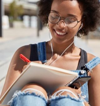 Uma menina ao ar livre estuda. O seu caderno está apoiado nas pernas enquanto ela tenta Calcular Nota do ENEM 2025