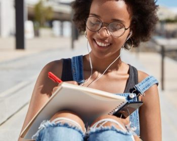 Uma menina ao ar livre estuda. O seu caderno está apoiado nas pernas enquanto ela tenta Calcular Nota do ENEM 2025