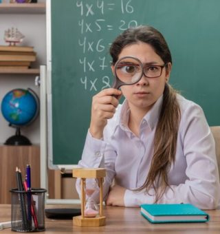 Uma professora sentada na sala de aula com uma lupa em frente ao olho