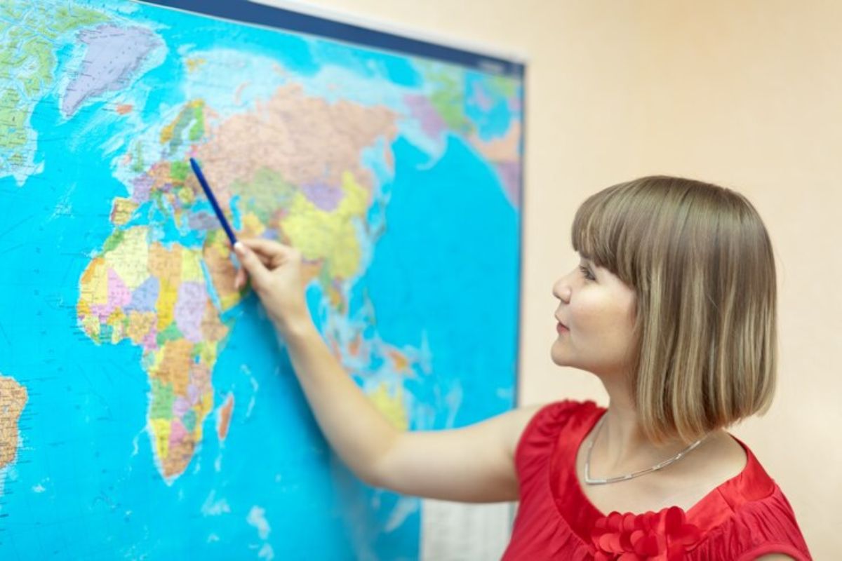 Uma professora aponta com o lápis para o Mapa-múndi