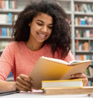 Uma aluna lendo um livro dentro da biblioteca após ver Cursos para Turbinar o Currículo e Mudar de Profissão em 2024