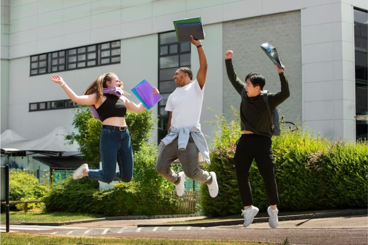 Três alunos pulando animados na saída da universidade