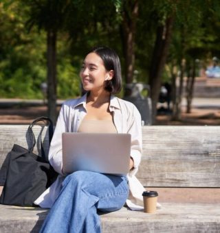 Uma menina sentada no banco da praça com o notebook no colo confere os detalhes da Transferência de Curso pelo FIES 2025