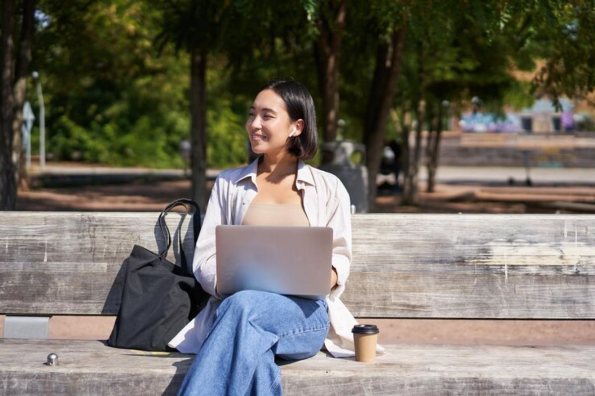 Uma menina sentada no banco da praça com o notebook no colo confere os detalhes da Transferência de Curso pelo FIES 2025