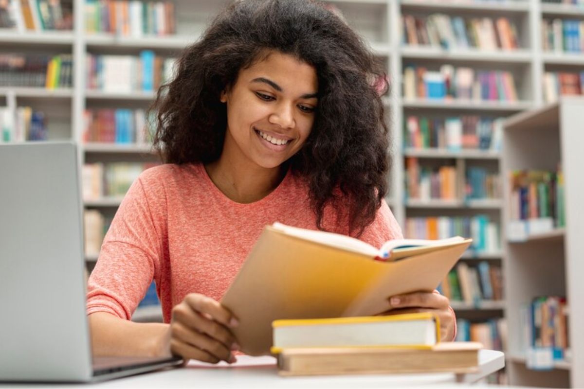 Uma aluna na biblioteca com um livro de capa amarela aberto