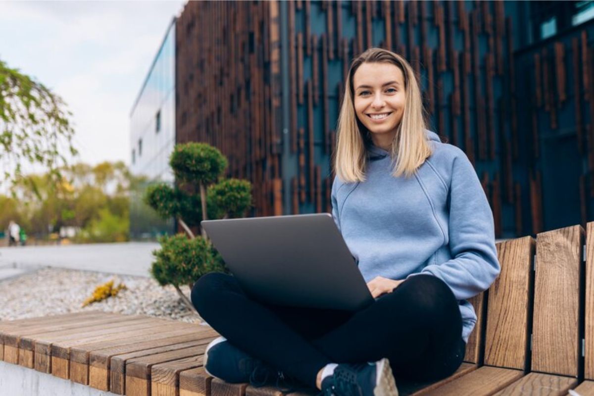 Uma aluna sentada na praça com o notebook no colo confere a Lista de Espera FIES 2025