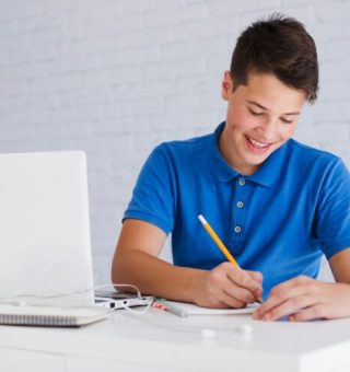 Um estudante faz anotações em seu caderno. Ele estuda em frente ao notebook, onde acessa o Caderno do Aluno 2025 Ensino Médio