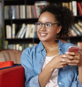Uma aluna dentro da biblioteca confere o Local de Prova ENEM 2025 pelo celular