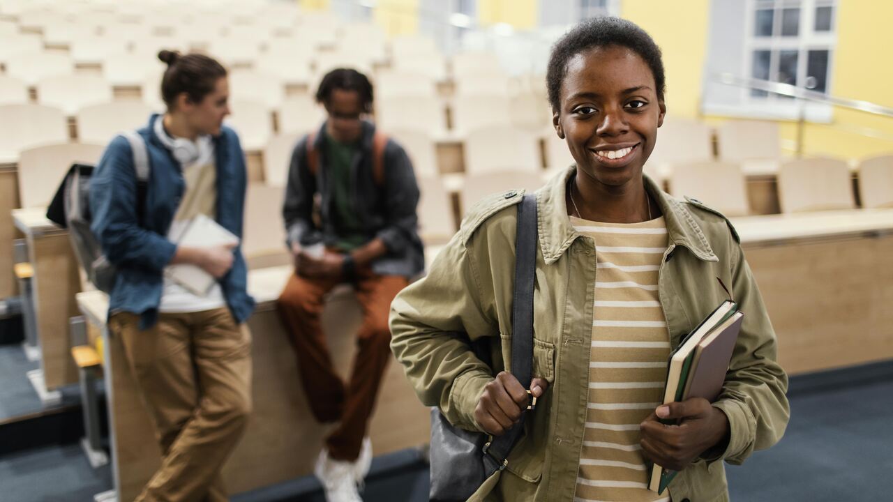 Estudante negra posa para foto na sala de aula com colegas ao fundo