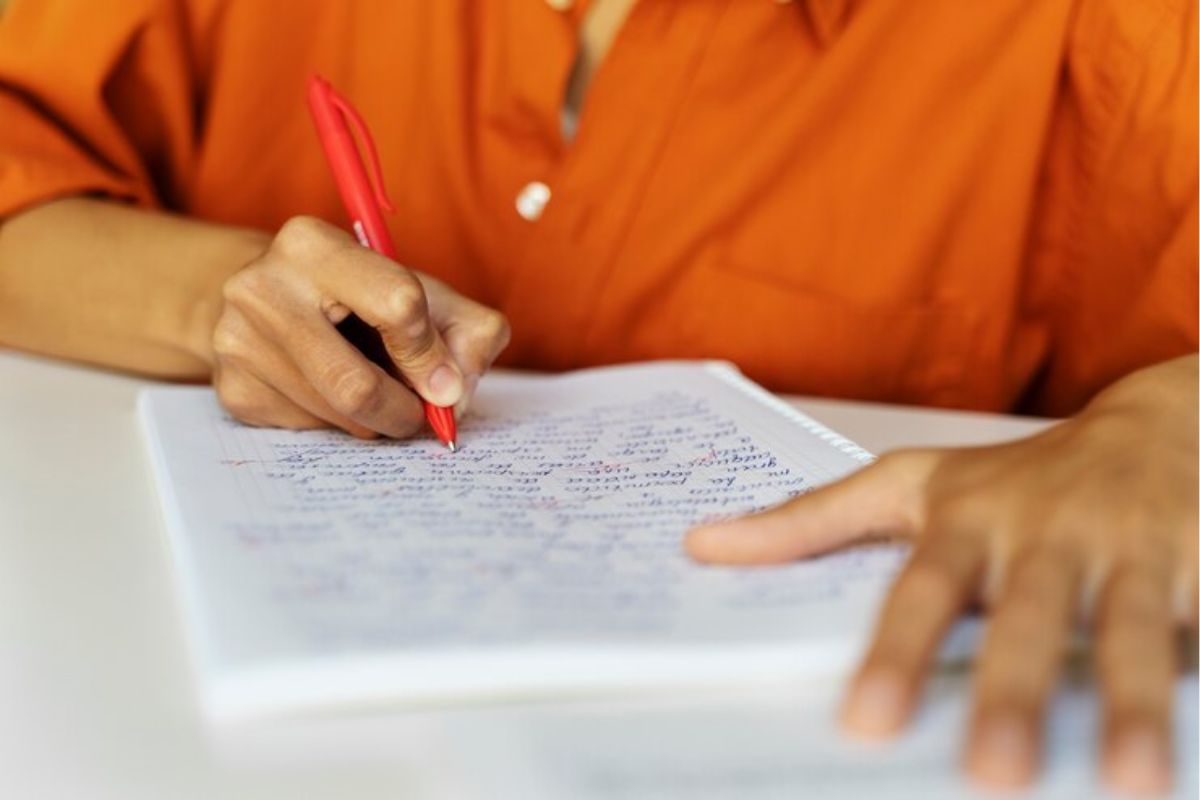 Uma pessoa de camisa laranja escrevendo uma redação após as Mudanças no ENEM 2025