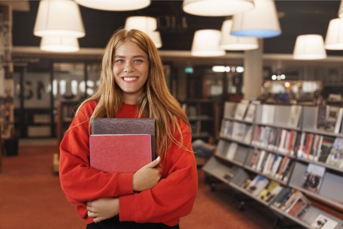 Uma menina na biblioteca segura o seu material no colo