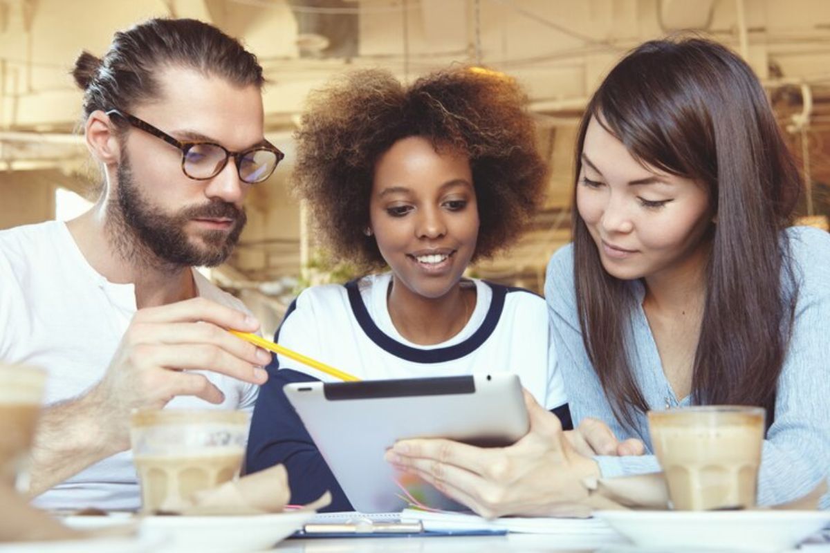 Três alunos juntos conferem os passos para o Pagamento do FIES 2025. Uma aluna segura um tablet enquanto outro faz um apontamento com um lápis