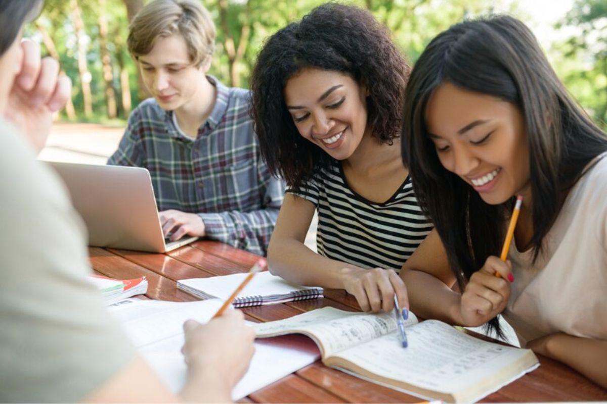 Um grupo de alunos ao ar livre na faculdade. Eles estudam juntos, sentados em uma mesa de madeira