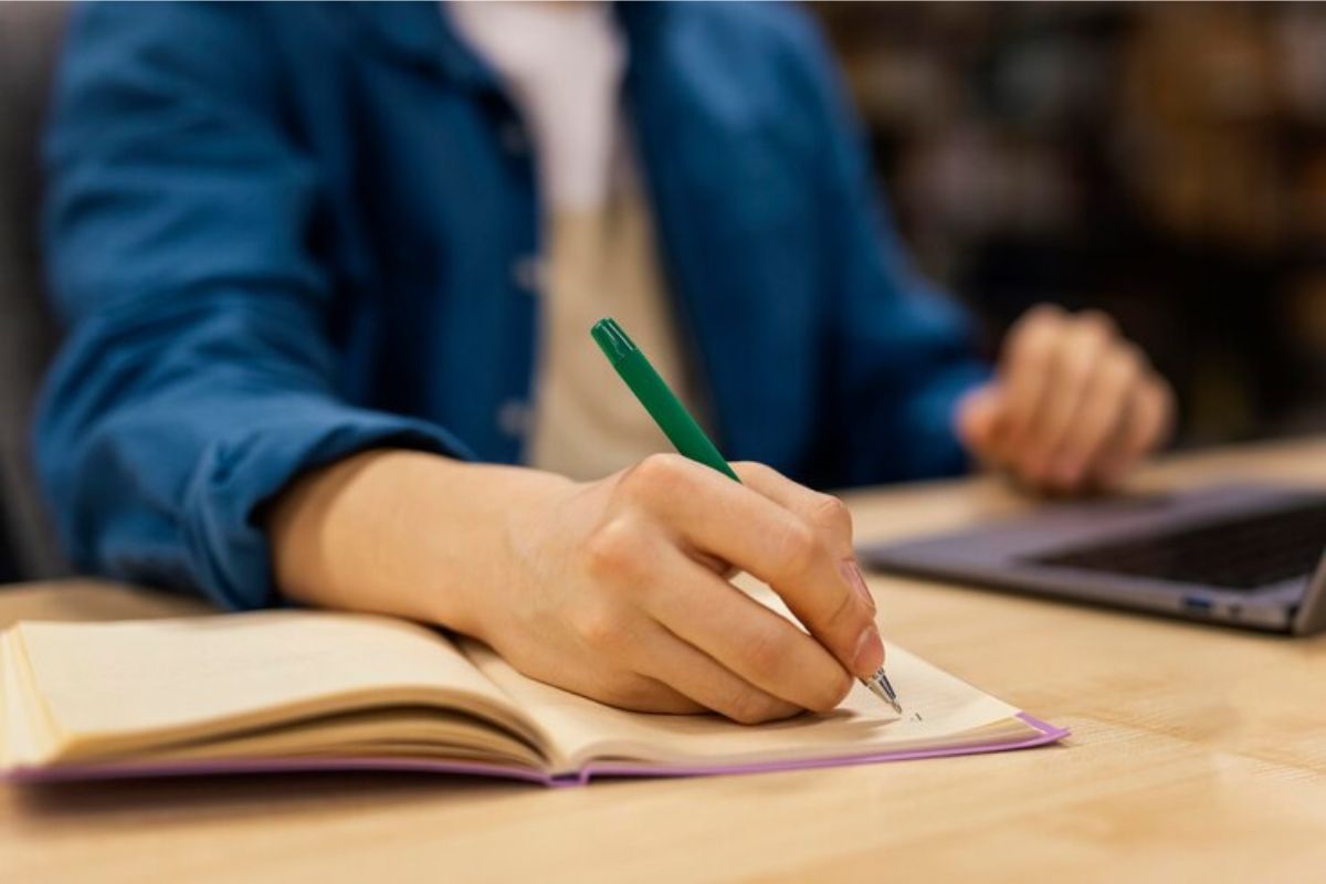 Uma pessoa faz anotação em seu caderno. Ela confere no notebook em sua frente os detalhes do vestibulinho ETEC segundo semestre 2025
