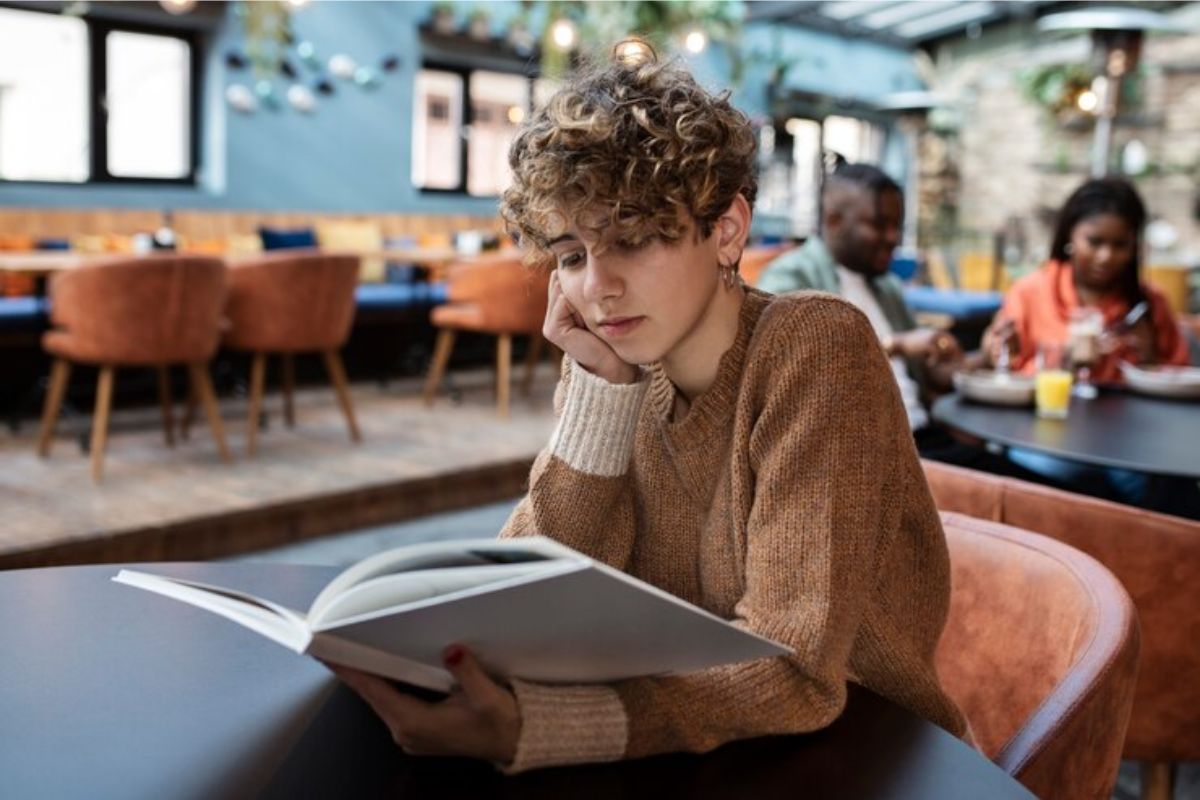 Uma menina olhando um livro sentada no refeitório. Ela procura Como Usar Nome Social no ENEM 2025