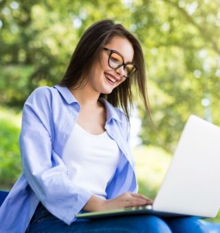 Uma mulher no jardim da universidade com notebook no colo vendo como Consultar Dívida FIES 2025