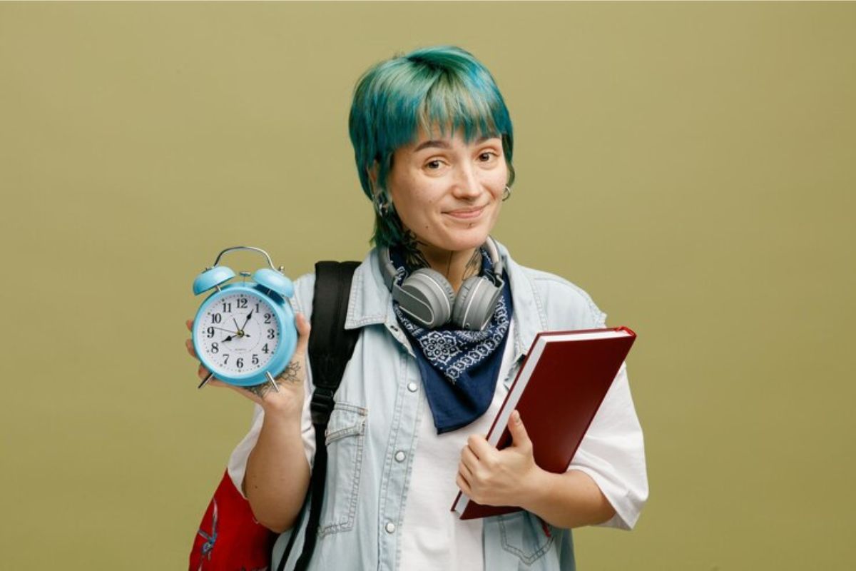 Uma menina de cabelo verde segura seu caderno e um despertador, indicando Quando Abrem as Vagas do Prouni 2025