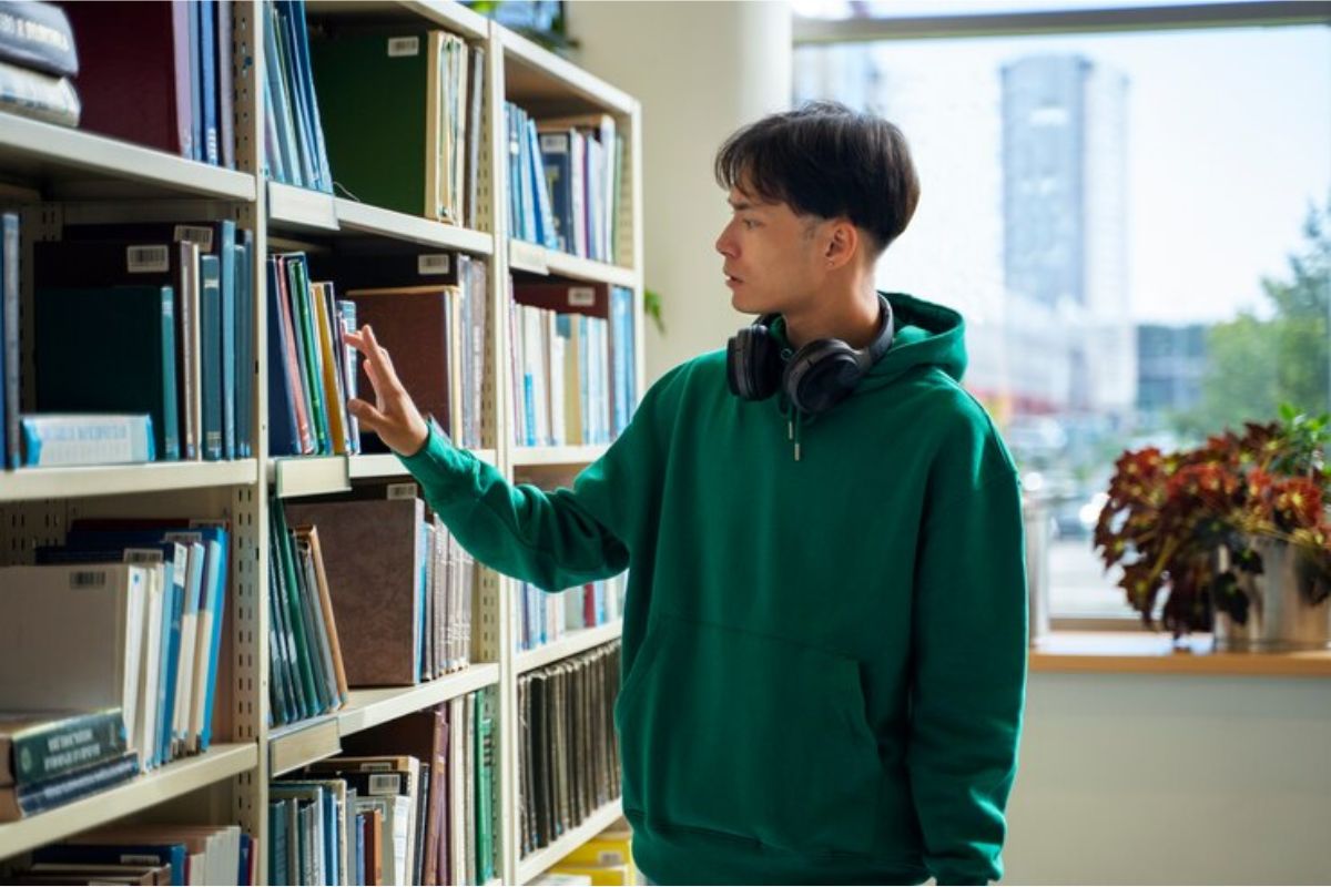 Um menino no corredor de uma biblioteca procura os Livros mais Cobrados no ENEM 2025