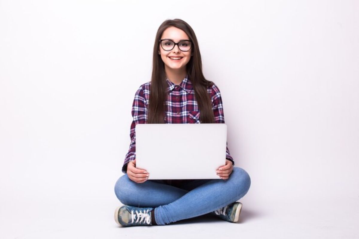 Uma estudante sentada com seu notebook no colo sorri para a foto