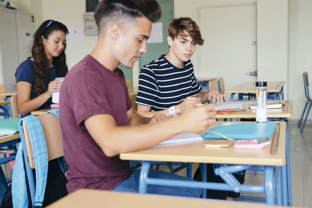 adolescentes fazem atividades sentados em suas mesas na sala de aula