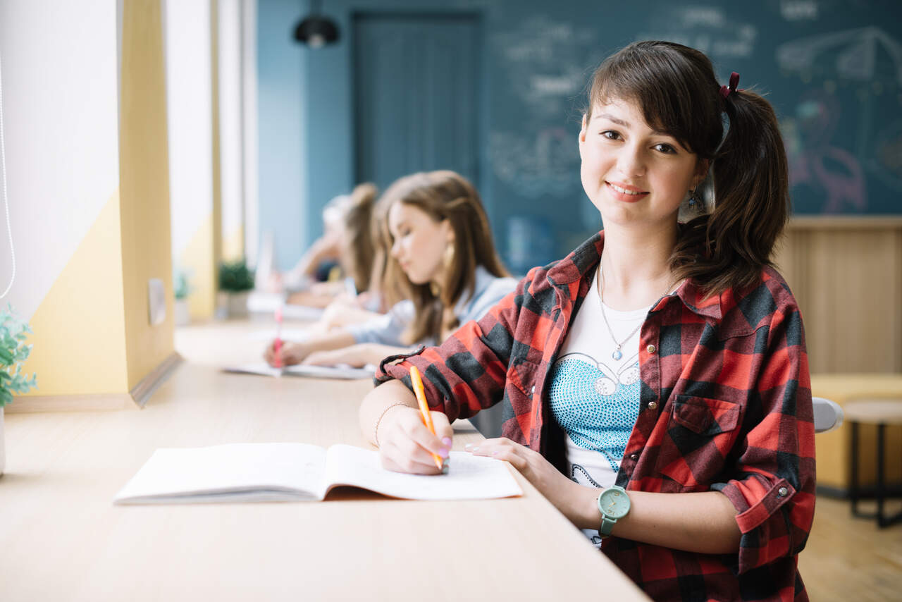 Adolescente posa sorridente enquanto faz sua lição na sala de aula