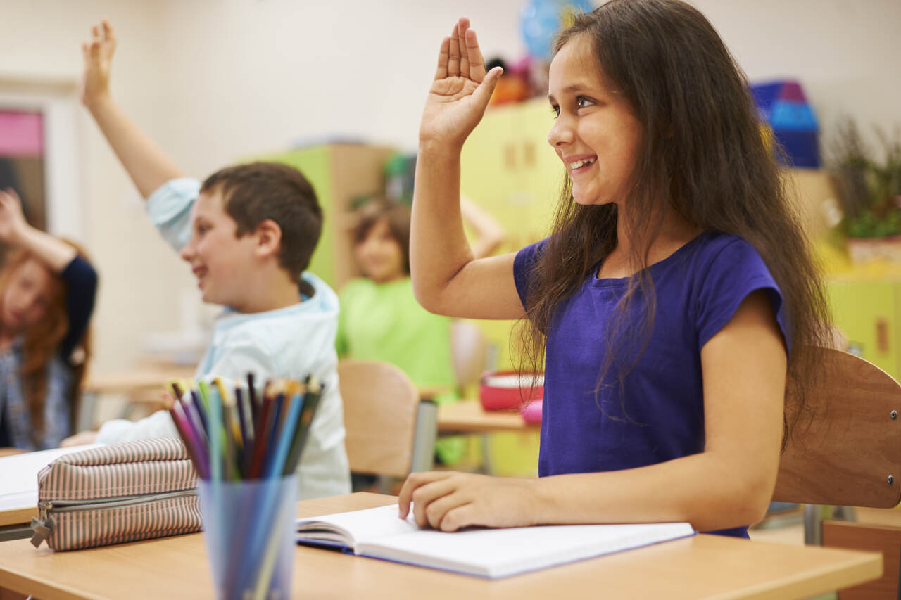 Crianças levantam a mão para responder professora na sala de aula