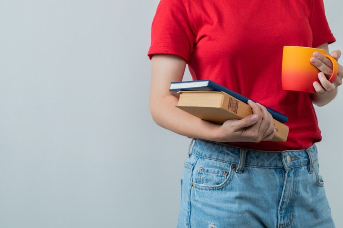 Uma estudante segura uma xícara em uma mão e na outra alguns livros