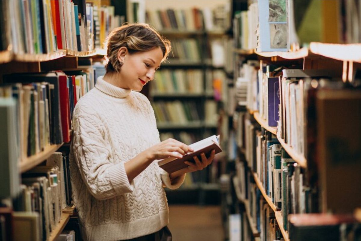 Uma jovem com o livro aberto no corredor da biblioteca 