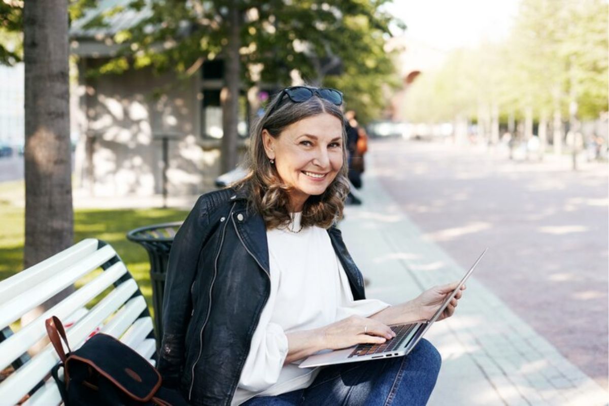Uma estudante da ETEC está sentada no banco da escola no jardim com seu notebook vendo os cursos ETEC que mais empregam 2025