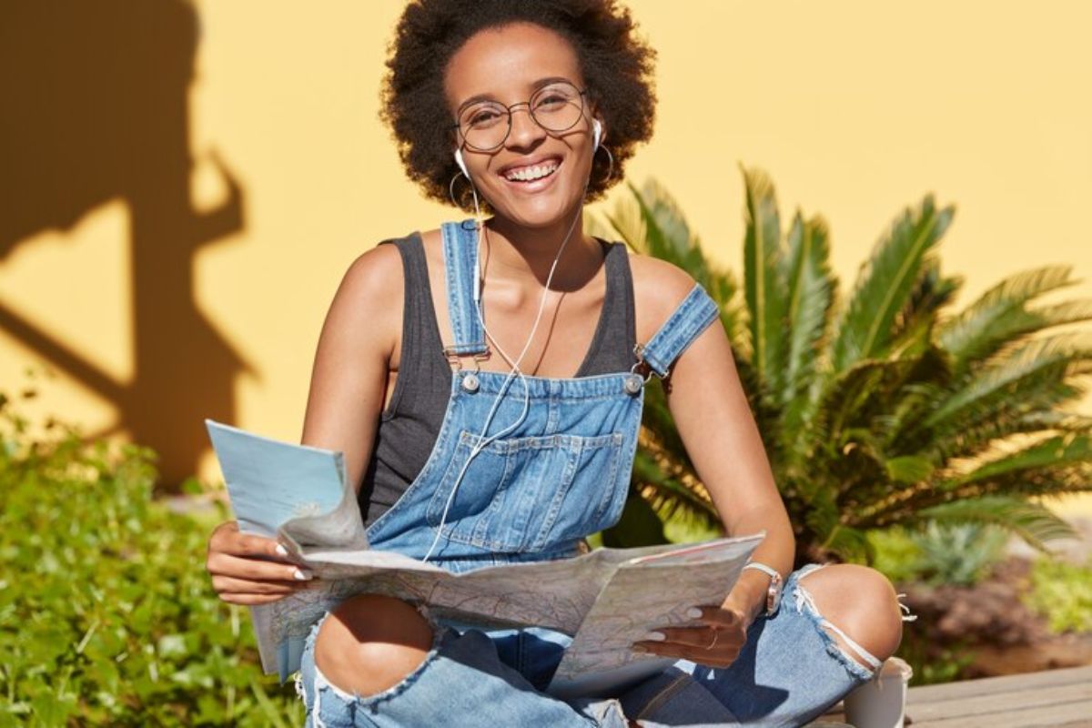 Uma aluna estuda ao ar livre com uma revista aberta em seu colo. Ela está sentada em uma mureta da escola