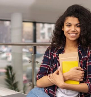 Uma estudante com o caderno contra o colo sorri após a isenção da taxa do ENEM 2024