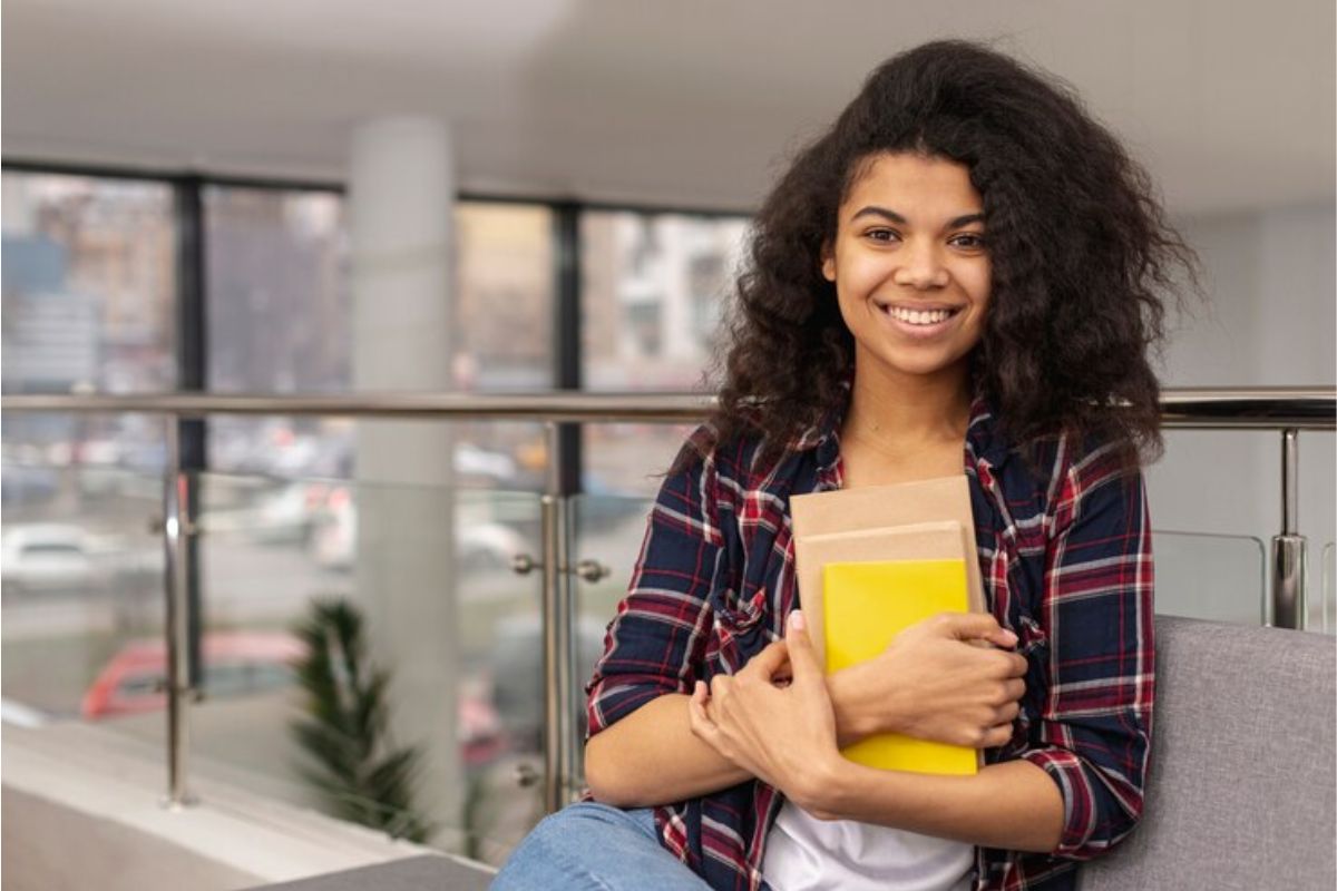Uma estudante com o caderno contra o colo sorri após a isenção da taxa do ENEM 2024