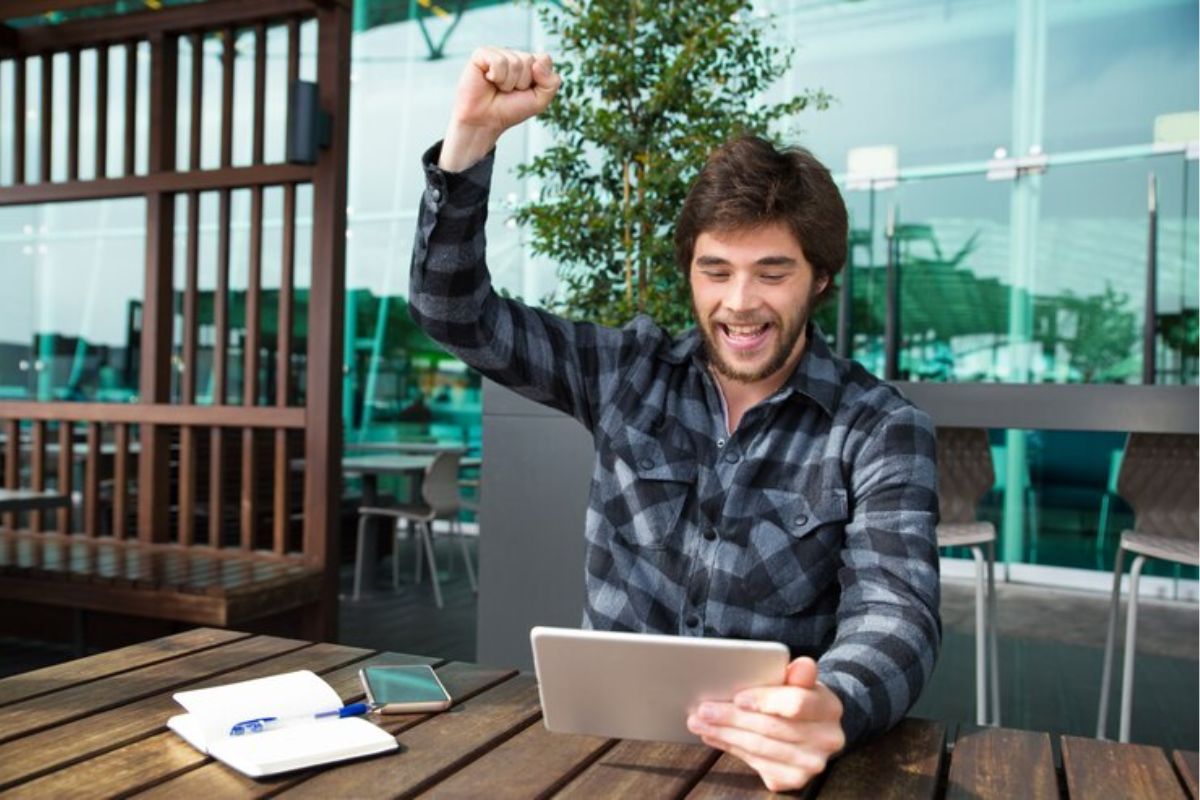Um jovem levanta o braço comemorando com um tablet na mão