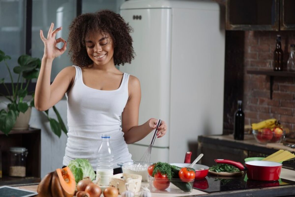 Uma mulher em frente à mesa cozinhando e fazendo sinal de Ok com a mão ─ aprenda a cozinhar 