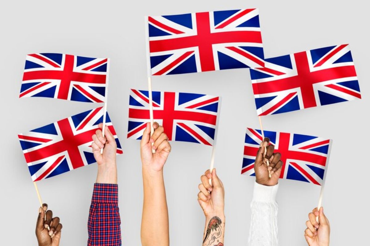 5 braços de pessoas aparecem segurando uma bandeira do Reino Unido. Elas participam dos cursos de idiomas gratuitos em SP