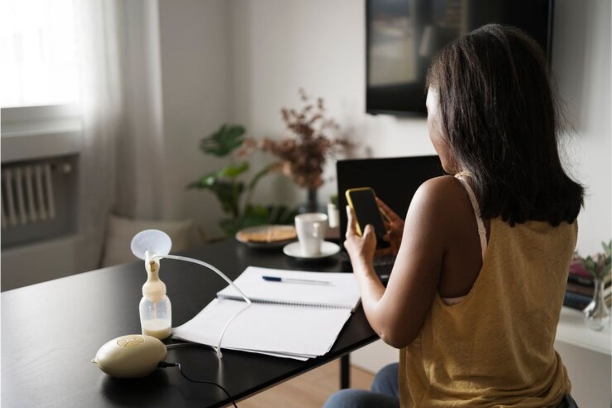 Uma estudante com o celular na mão. Ela está de costas para a foto. Em sua frente está a mesa onde ela olha o notebook e tem um caderno na mesa enquanto ela participa da Harvard Cursos Gratuitos 2024