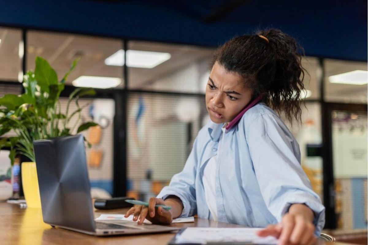 Uma menina no escritório em frente ao notebook e falando no celular. Ela participa do programa Jovem Aprendiz Barra Mansa 2024