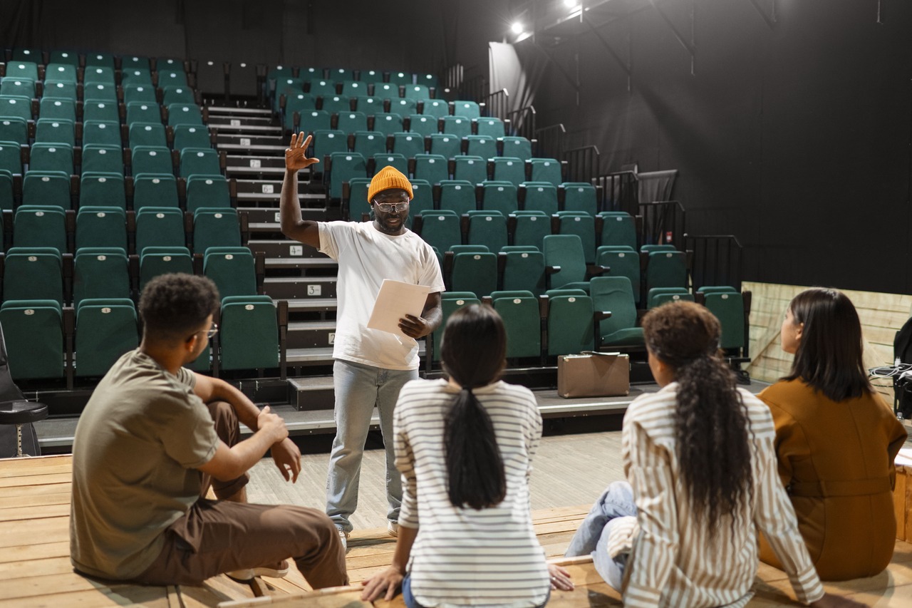 Professor de teatro orienta alunos sentados a sua frente