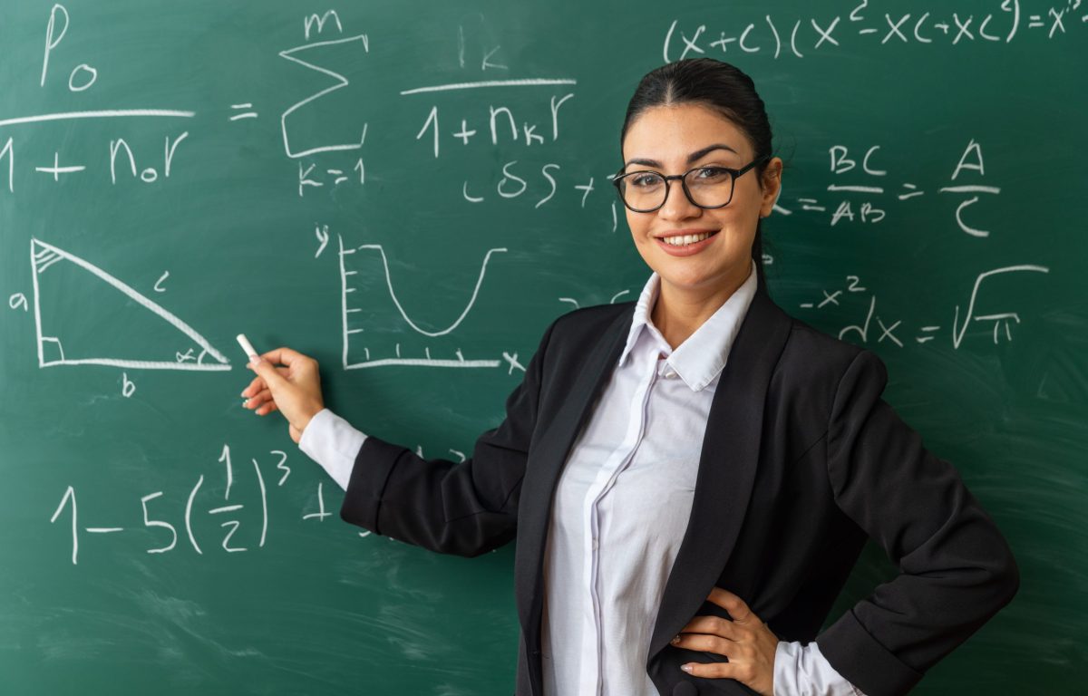 Professora sorridente posa enquanto escreve na lousa 